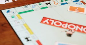 Close-up of people playing Monopoly, showcasing board and game pieces on a wooden table.